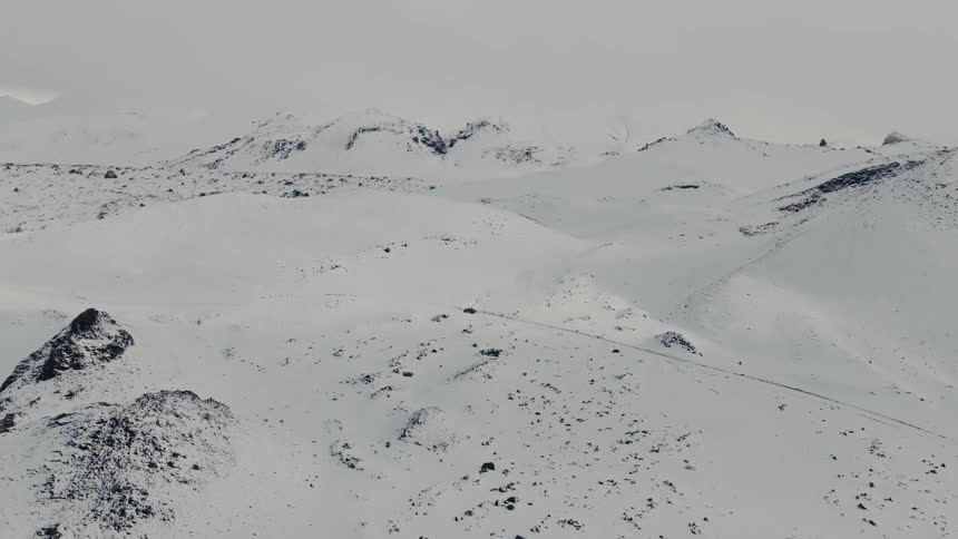 A lone car drives through a vast, desolate snow-covered mountain landscape in this epic aerial shot