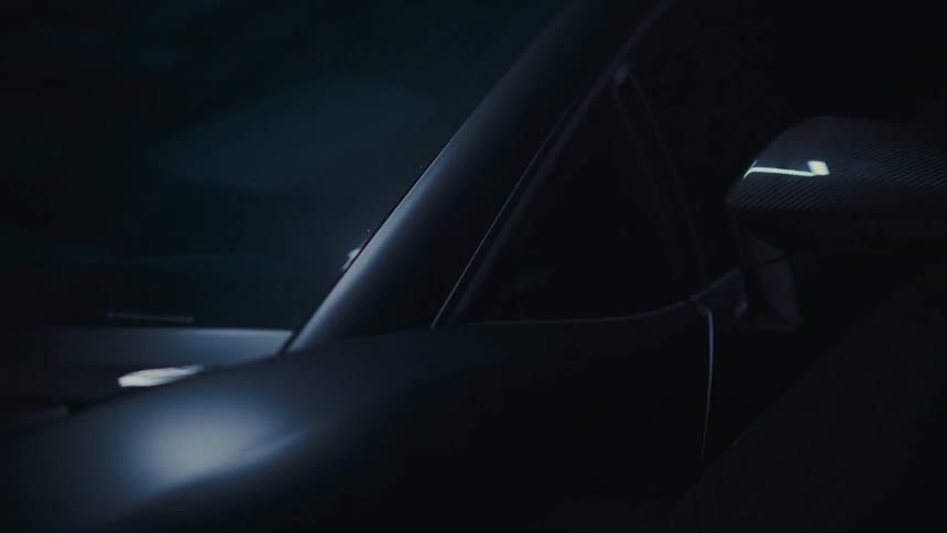 A close-up shot of a sleek, dark sports car in a moody setting as its side mirror turn signal illuminates