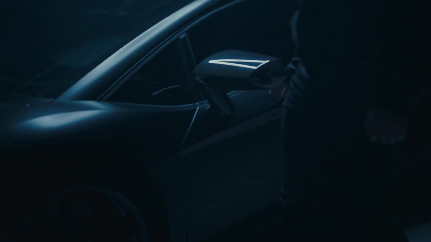 Slow pull-back shot reveals a modern sports car with a person standing beside it in a dark, moody environment