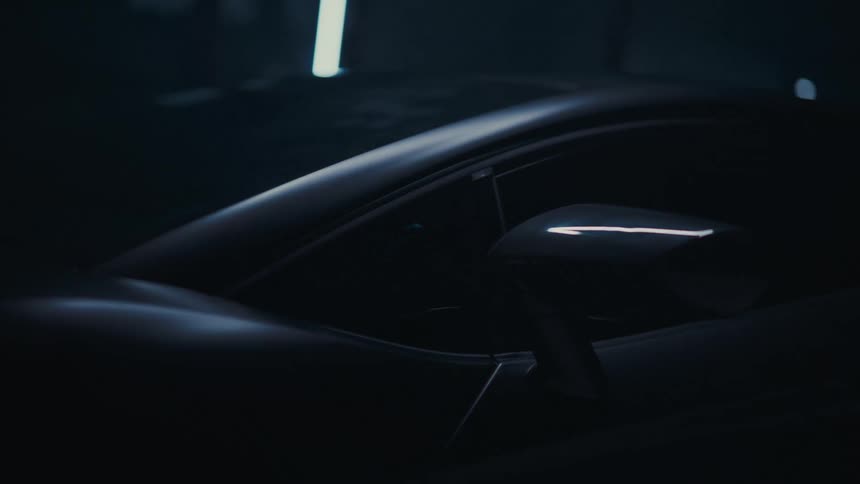 Close up of a sleek, luxury sports car's side mirror and body as a soft light highlights its curves in a dark garage