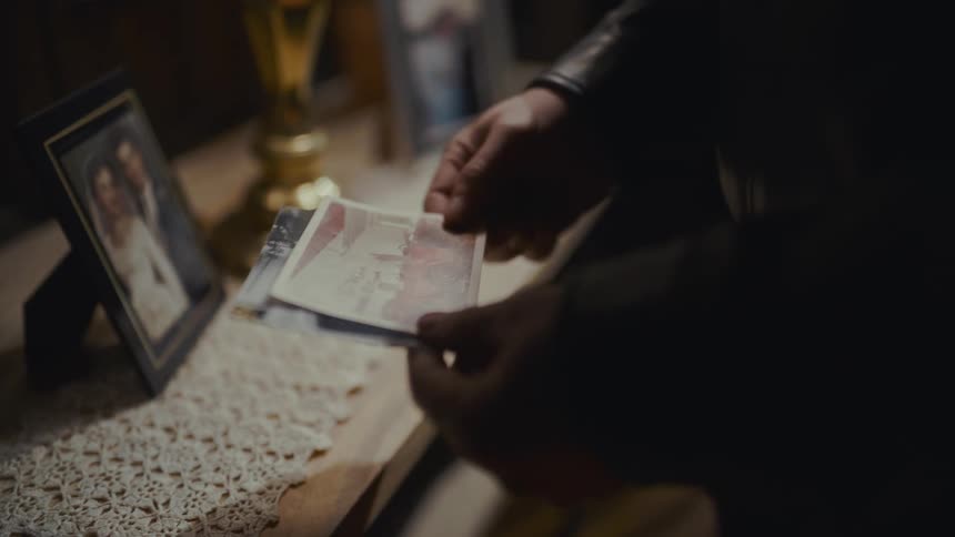 A person sentimentally reminisces while looking through old photographs in a dimly lit room