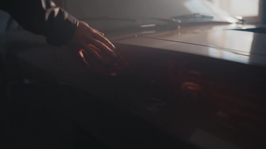 A close-up shot of a hand gently caressing the side of a classic car in a smoky, dramatically lit garage