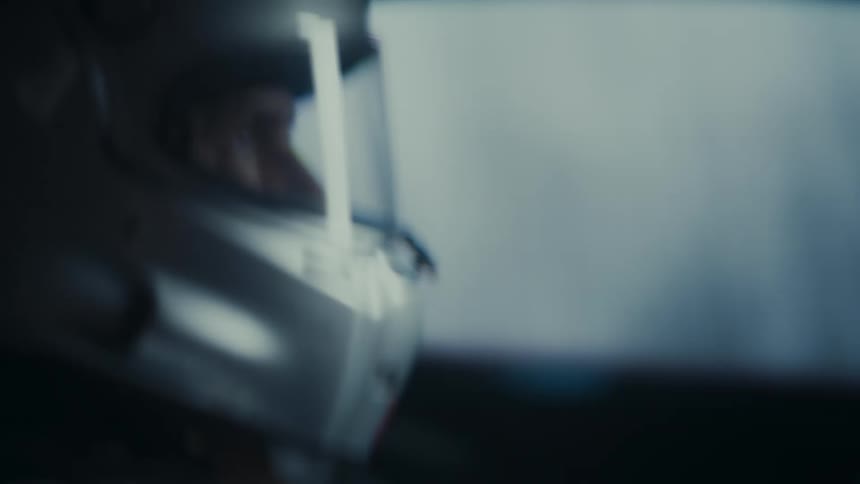 A shaky, handheld close-up of a race car driver's silver helmet as they drive at high speed in a dark environment