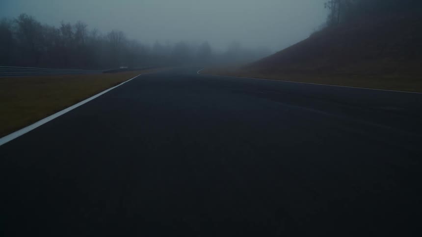 A moody first-person perspective driving along a desolate, winding racetrack enveloped in thick fog