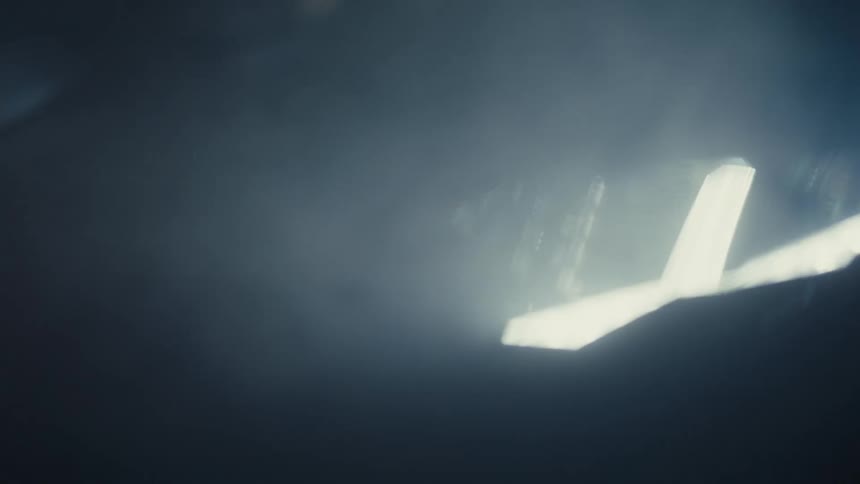 A shaky, handheld close-up shot captures a modern car's LED headlight cutting through thick fog at night