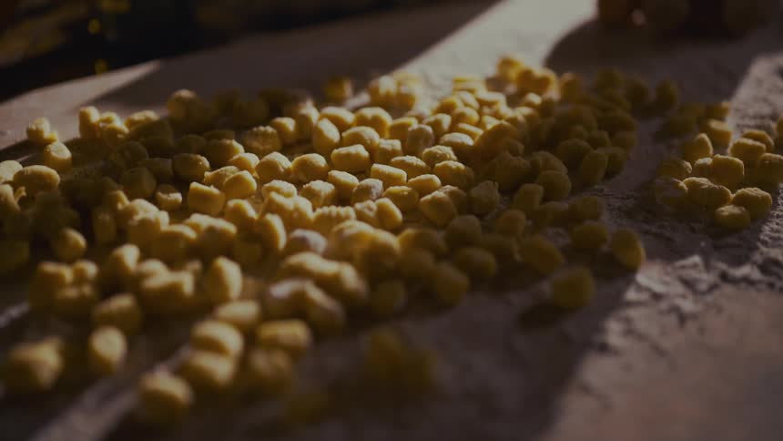 A close-up shot of freshly made gnocchi resting on a floured wooden surface in the warm sunlight