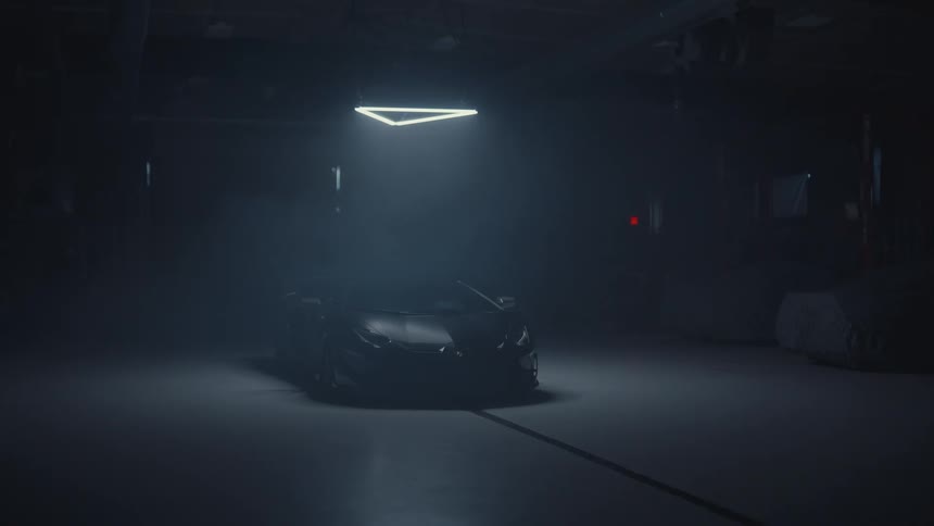 A sleek black Lamborghini sits in a dark, hazy warehouse under a single spotlight before its headlights turn on