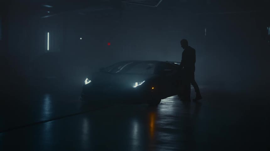 A man walks up to and opens the door of his luxury sports car in a dark, smoky garage at night