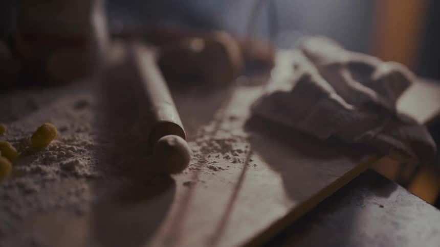 A slow-motion close-up pan across a rustic, flour-dusted countertop with baking ingredients and tools under dramatic backlighting