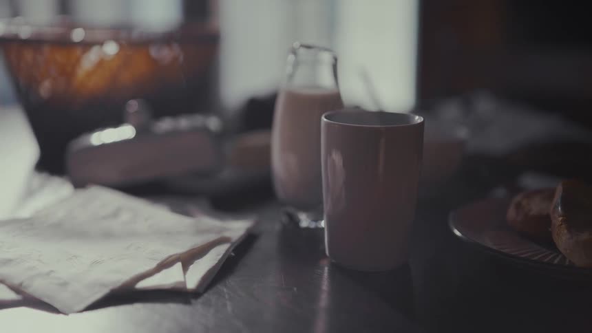 Steam rises from a warm beverage on a cozy, dimly lit breakfast table