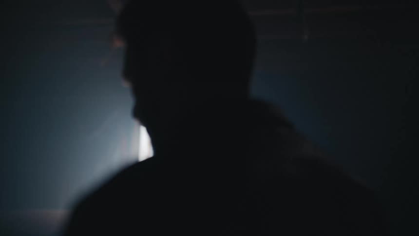 Cinematic slow motion shot of a man in a leather jacket silhouetted by a bright light in a dark, moody room