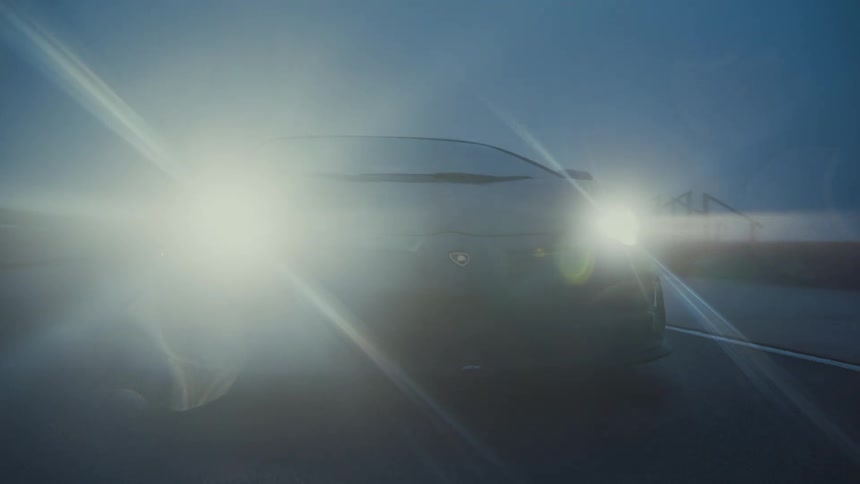 A black supercar's headlights flare up, illuminating the dense fog on a wet road at night
