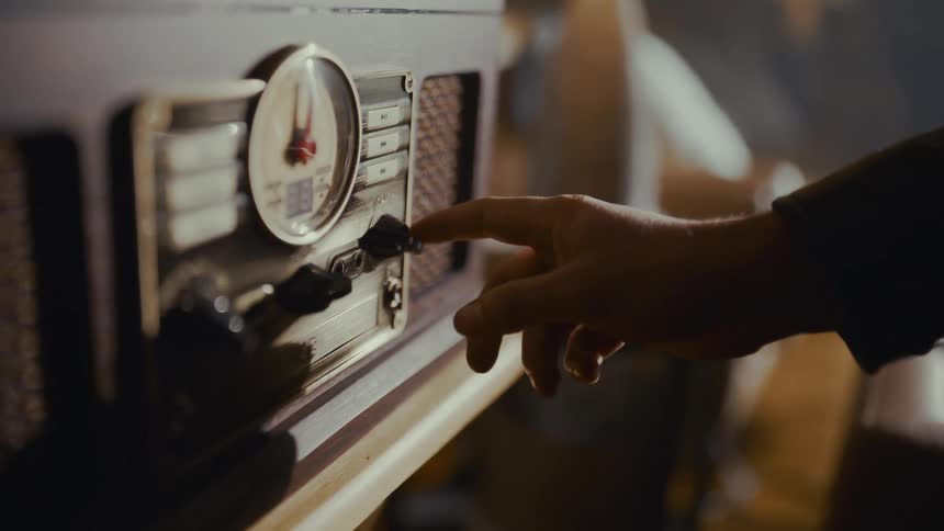 A close-up shot of a hand turning the knob on a vintage-style radio player