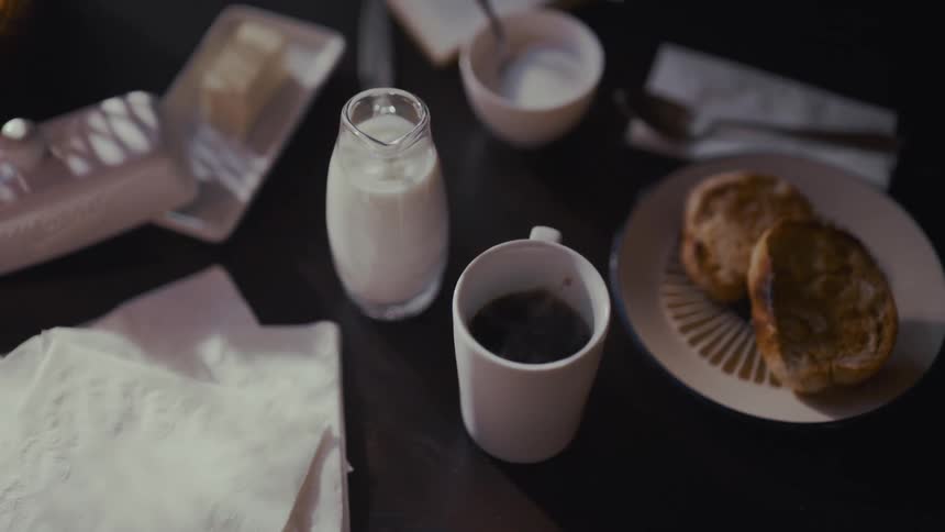 A drop of milk splashes in slow motion into a pitcher during a moody and quiet morning breakfast