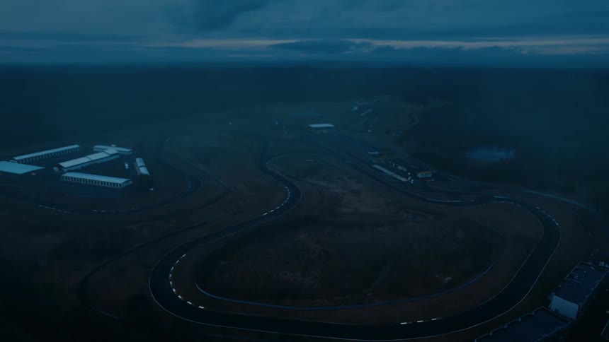 An atmospheric aerial view slowly approaches an empty, winding race track at twilight