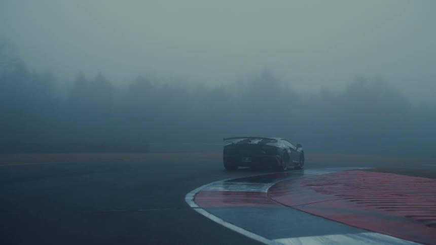 Following a black supercar as it slowly drives around a racetrack corner and disappears into the thick, moody fog