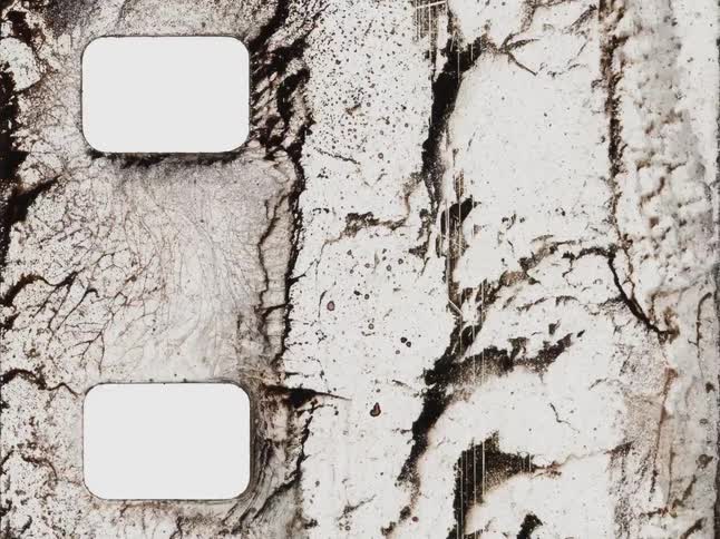 Close up of an old, damaged film strip with sprocket holes showing various burn marks and decay in a stop motion animation