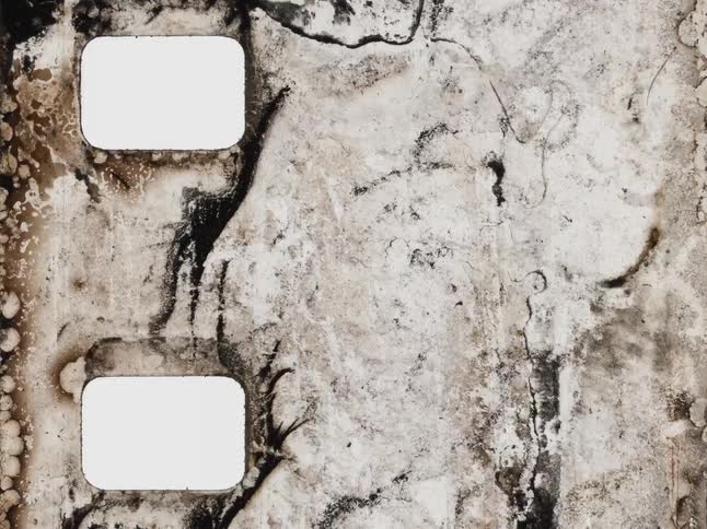 An abstract stop-motion animation shows the decaying and burning texture of an old, damaged film strip with blank frames