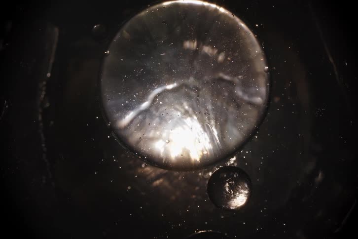 A macro shot of metallic, silvery liquid bubbles slowly morphing against a dark background, creating a cosmic effect