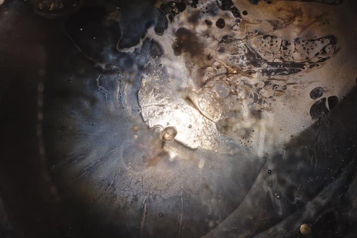 An otherworldly macro shot of dark, iridescent liquids bubbling and evolving in slow motion