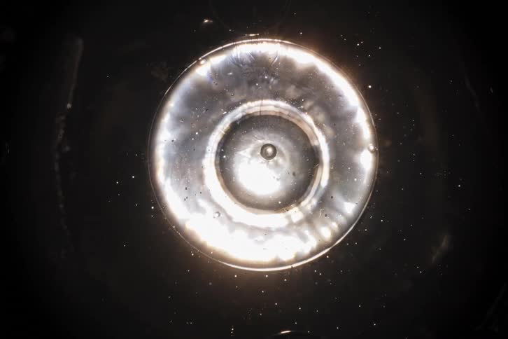An abstract macro shot shows a bright circular light distorting and swirling within a dark, particle-filled liquid