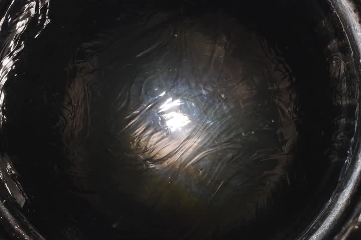 An abstract, top-down view captures the mysterious reflection of a bright light on the still surface of dark water