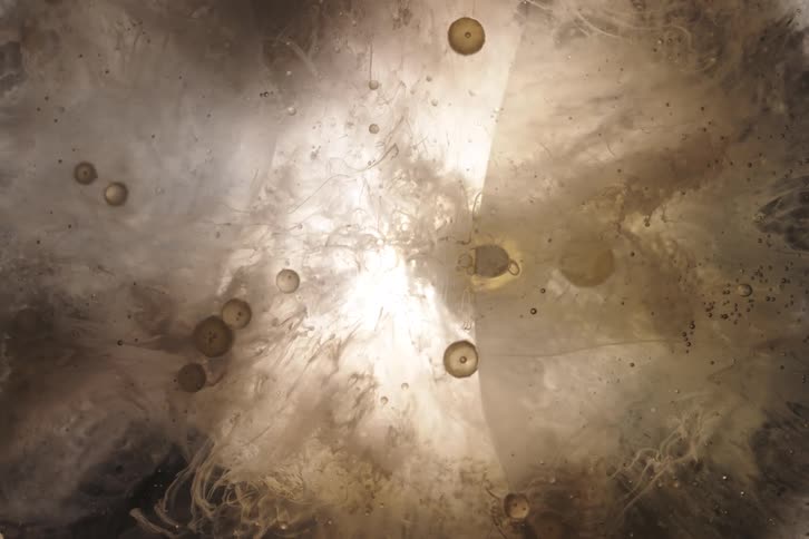 Ethereal, murky liquid swirls with golden bubbles around a bright light source in an abstract macro shot