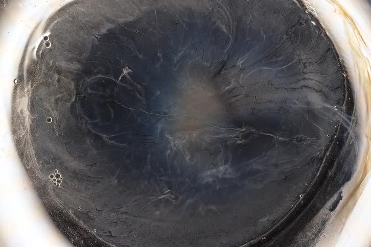 Dark, smoky liquid swirls and evaporates over time, leaving behind a dry, cracked surface in a macro time-lapse
