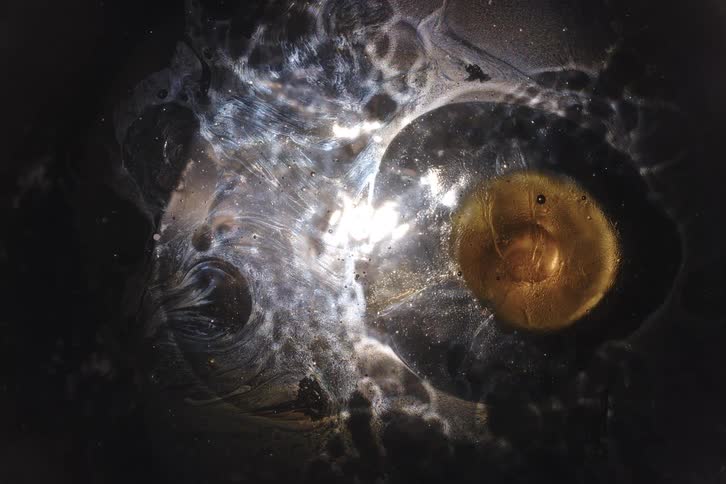 A golden planet dissolves in a shimmering silver nebula against a dark cosmic background