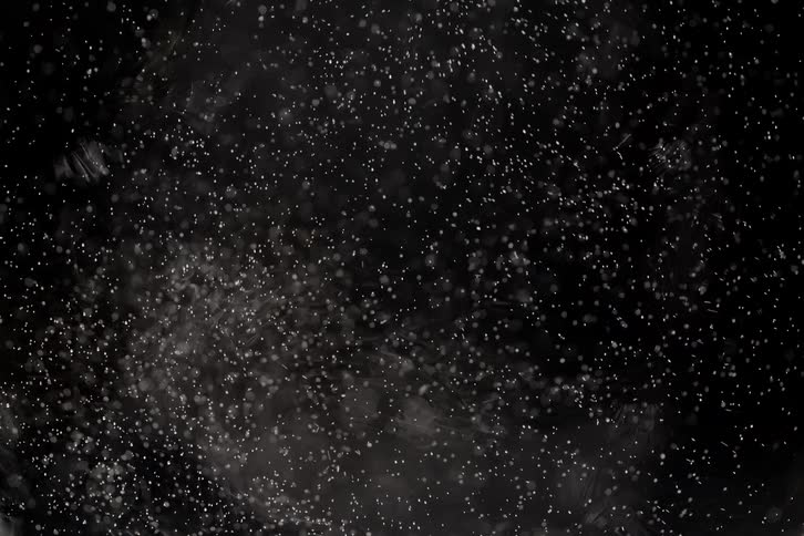 A mesmerizing slow motion shot of tiny white particles floating and swirling against a dark background