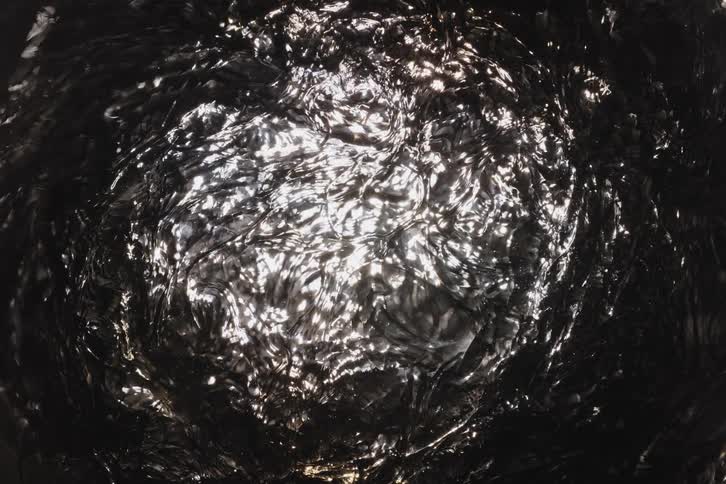 A mesmerizing abstract view of sunlight shimmering and reflecting on the surface of dark, gently rippling water