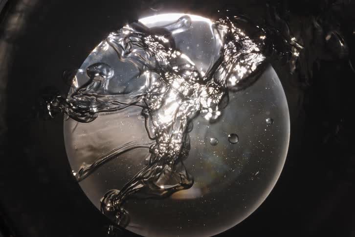 Mesmerizing close-up of a thick transparent gel-like liquid shimmering as it reflects bright light against a dark background