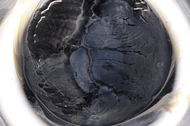 Mysterious white smoke-like fluid slowly dissipates, revealing a dark, cracked, and textured circular mass