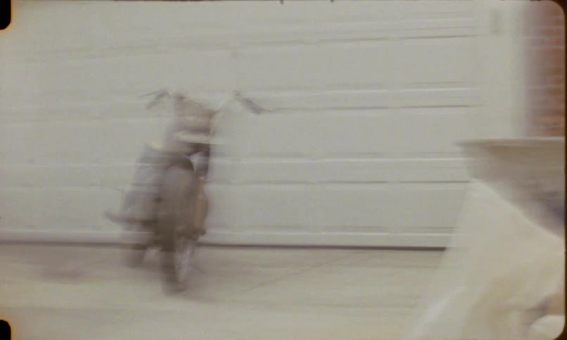 Chaotic and shaky archival footage flashes images of a vintage motorcycle in a driveway