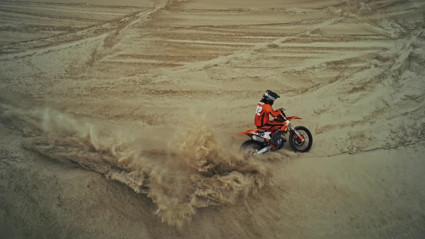 Cinemagraph of a motocross rider revving a dirt bike's engine, kicking up a huge cloud of sand
