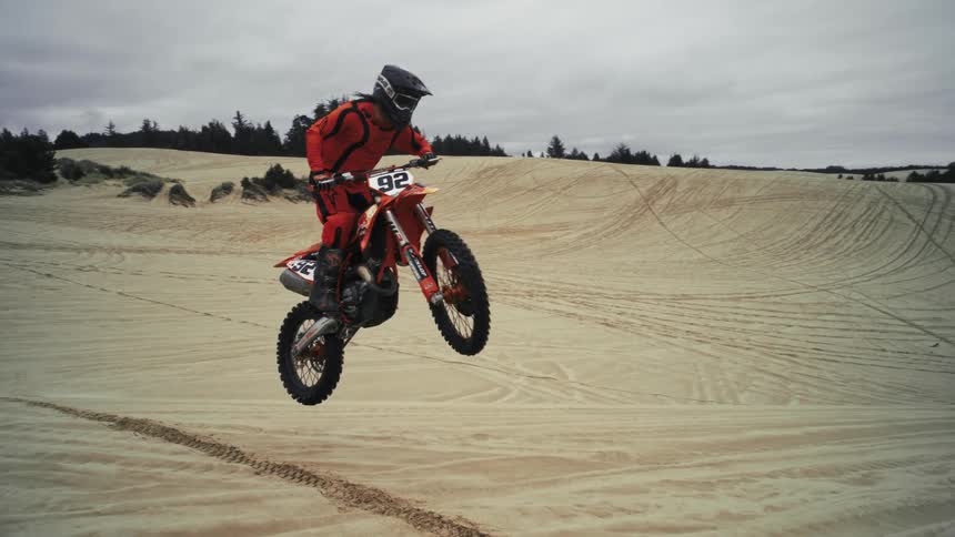 A motocross rider in full gear gracefully jumps over a sand dune in extreme slow motion