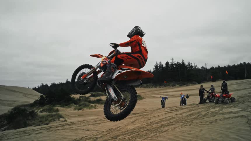 A motocross rider hangs in the air while performing a stunt on sand dunes as the camera pans around in slow motion