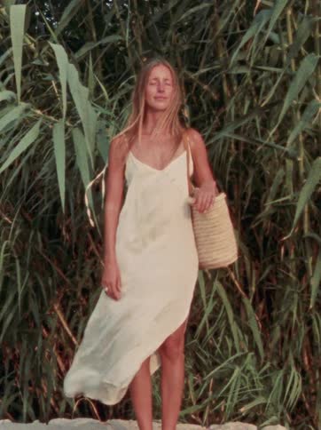 A serene woman with her eyes closed enjoys the gentle breeze while her dress flows in the wind