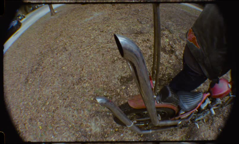 A fisheye view of a person sitting on a custom chopper motorcycle with long exhaust pipes, parked on a bed of autumn leaves