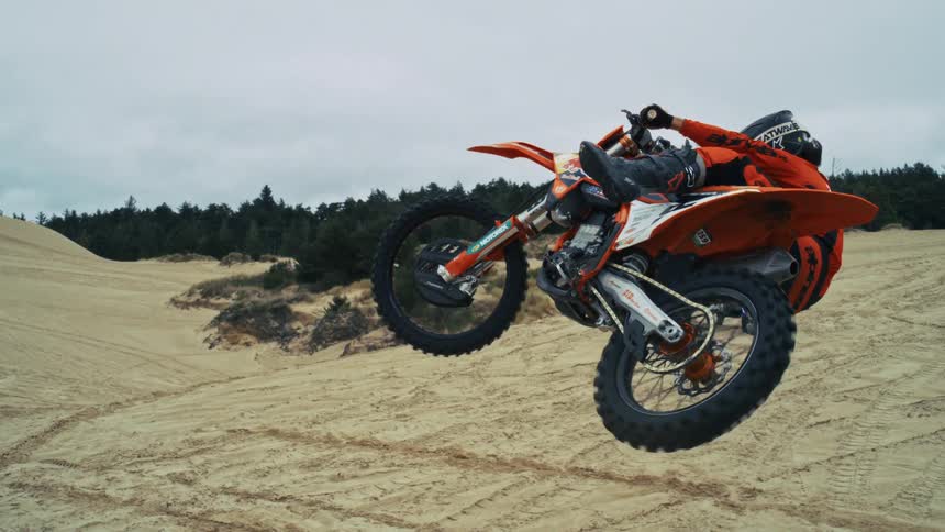 A professional motocross rider is frozen in time while performing a trick mid-air over a sand dune in this cinemagraph