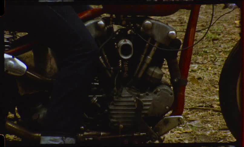 Close up of a classic red chopper motorcycle engine zooms out to reveal a biker sitting on the bike in a gritty outdoor setting