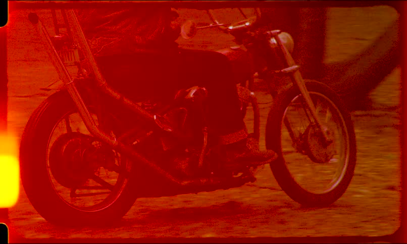 A biker rides a vintage red chopper motorcycle past a graffiti wall with an authentic old film look and feel