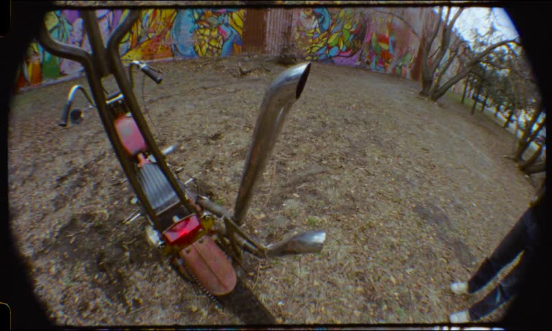 High-angle fisheye view of a custom chopper motorcycle parked on the ground in front of a vibrant graffiti wall