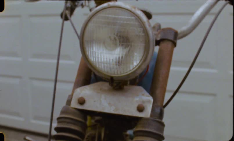 A close-up tilt shot of a vintage rusty motorcycle, moving from the front tire up to the headlight and handlebars