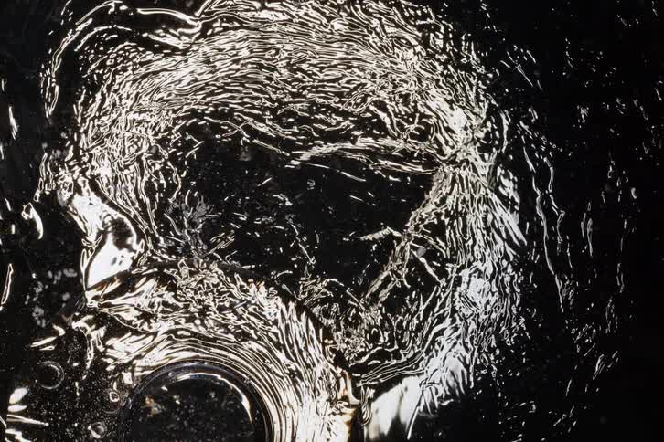 A mesmerizing top-down view of shimmering, silvery liquid swirling chaotically on a dark surface