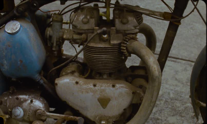 Close-up, vintage-style footage pans across the details of an old, rusty, and derelict blue motorcycle