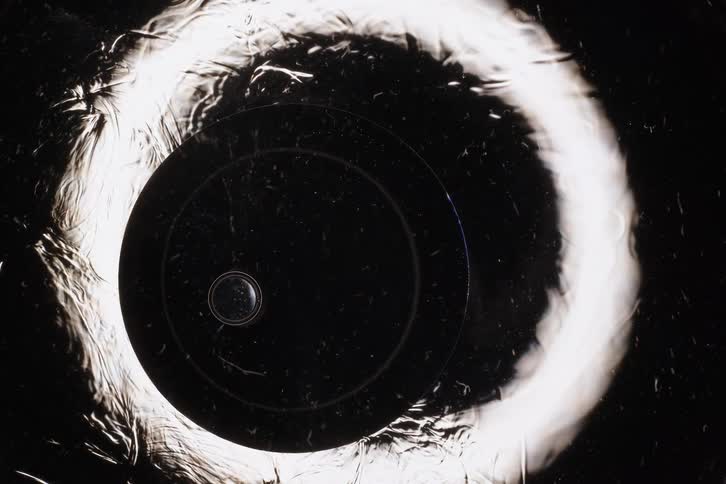 Mysterious abstract celestial bodies align, showing a bright, textured eclipse against a dark background
