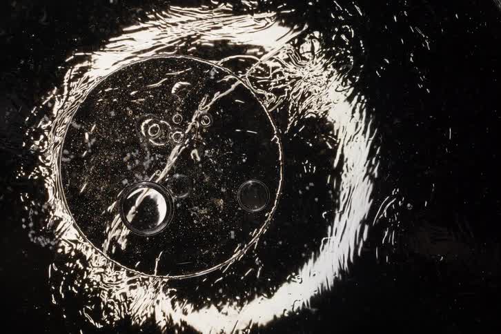 Abstract macro view of a luminous, oily liquid with bubbles slowly spreading across a dark surface