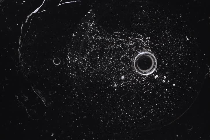 An abstract macro shot of bubbles and particles resembling a cosmic galaxy slowly moving in a dark liquid