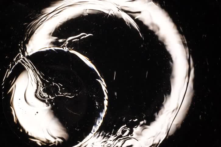 Monochromatic macro shot of a clear gel-like substance slowly shifting and melting against a dark surface